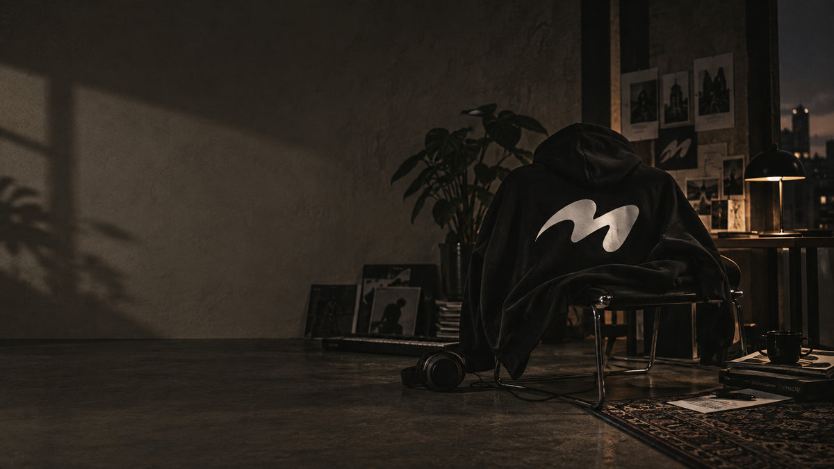 A black melowear hoodie with the symbol printed large across the back, draped over a chair in a dark room